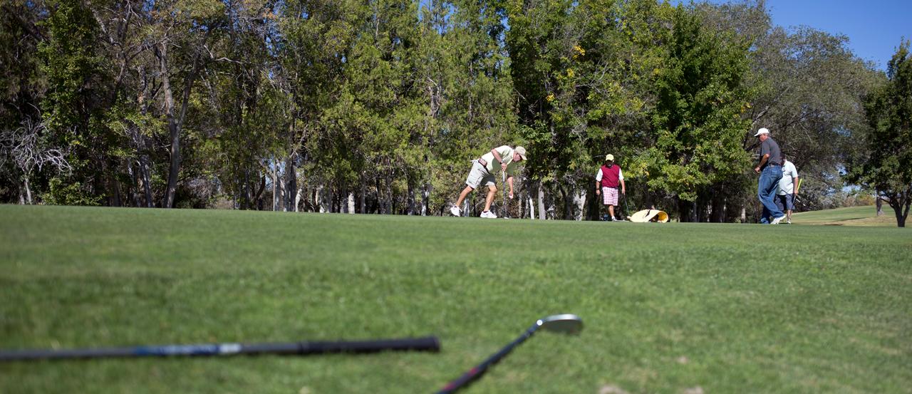 Image of four golfers in the distance, close up of golf clubs on the ground